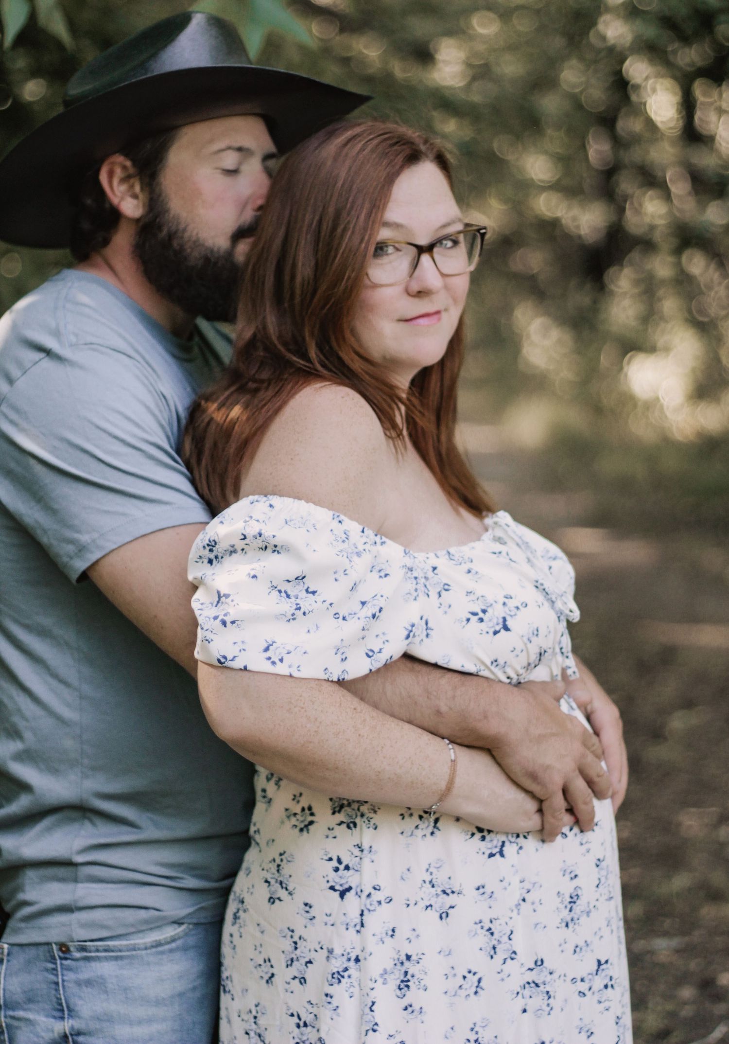 A couple embraces tenderly while wearing casual clothing in a sunlit outdoor setting.
