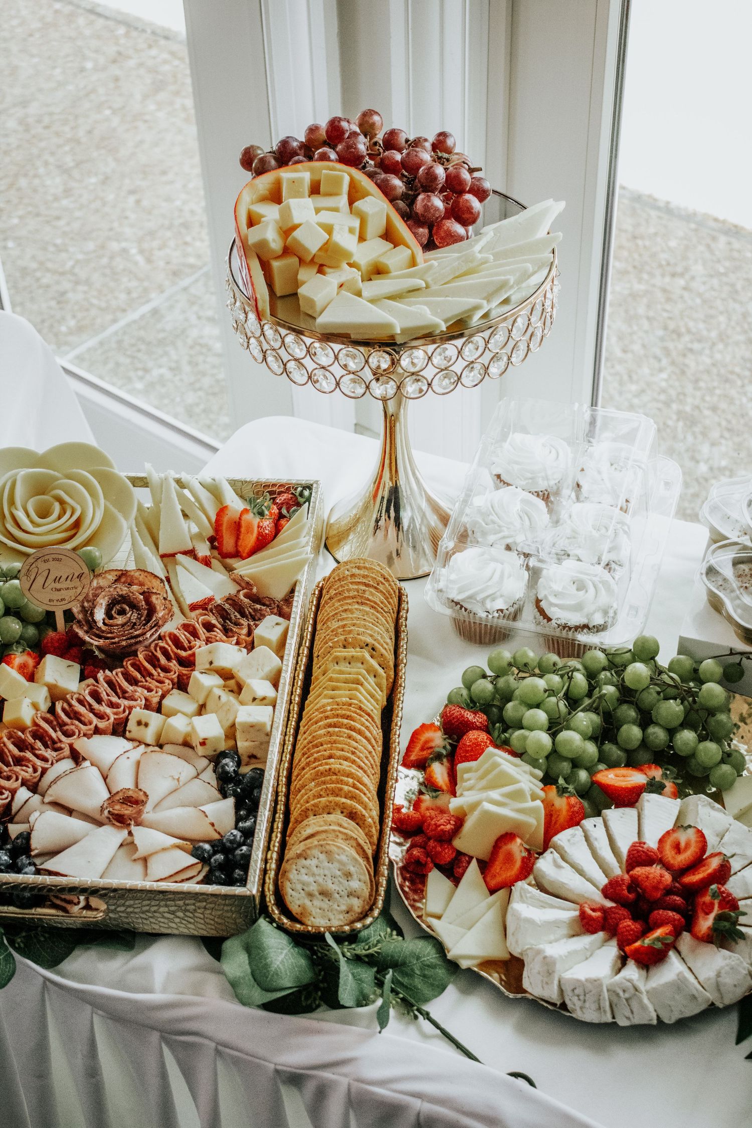 Gourmet cheese and fruit display on gold stands with crackers and fresh strawberries.