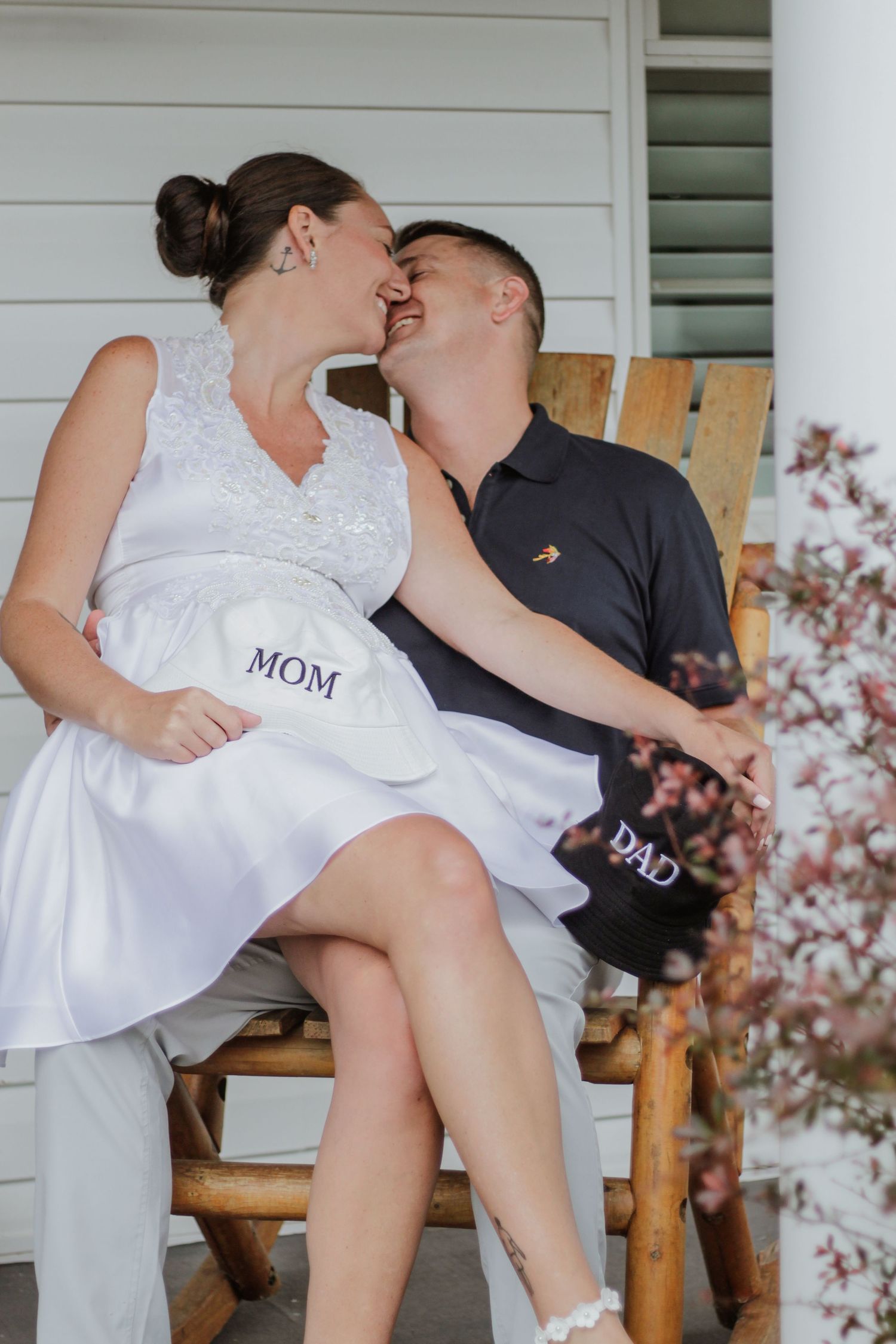 Couple in wedding attire sitting on porch chairs labeled 'MOM' and 'DAD'.