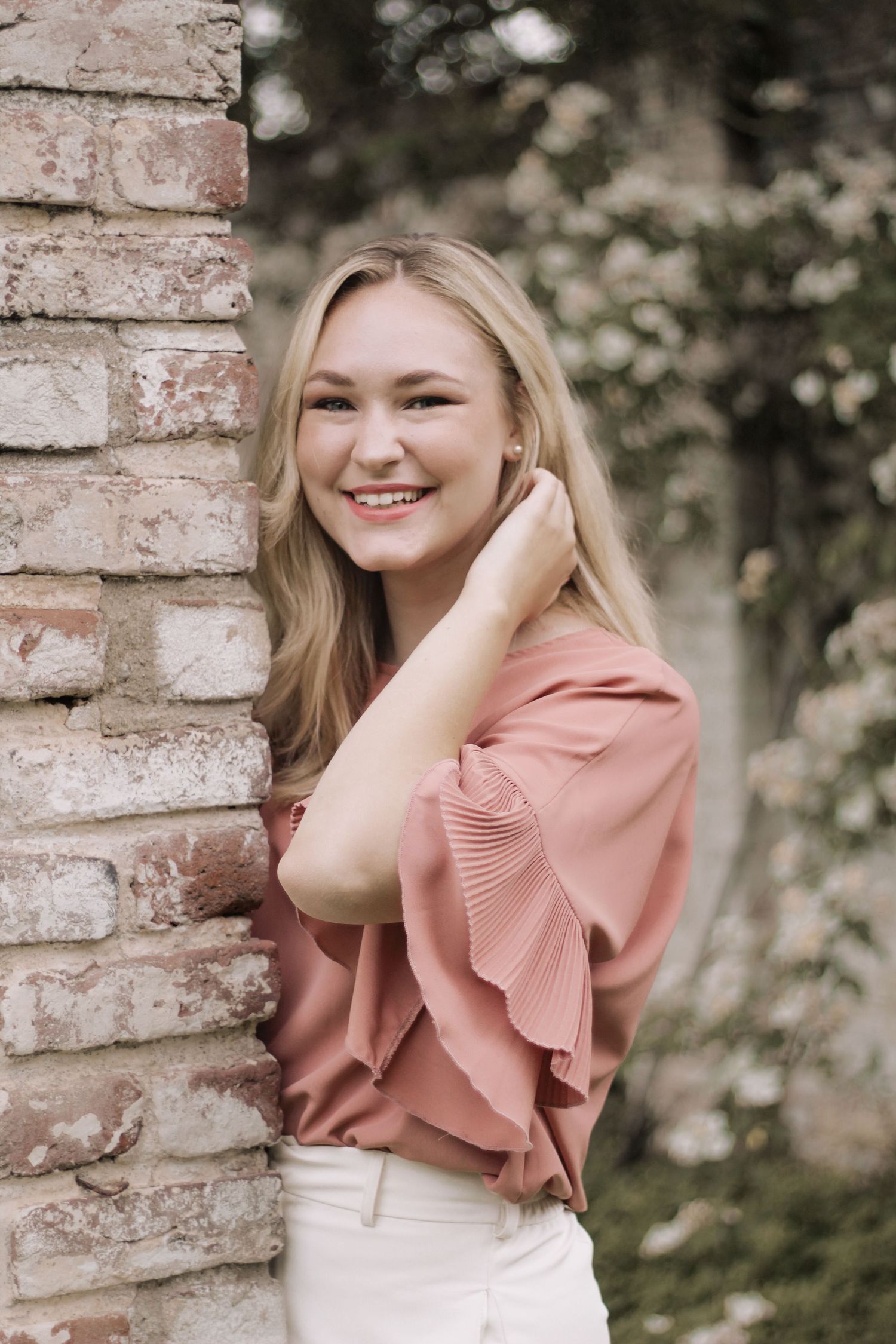 Portrait series in pink ruffle top against rustic brick backdrop.
