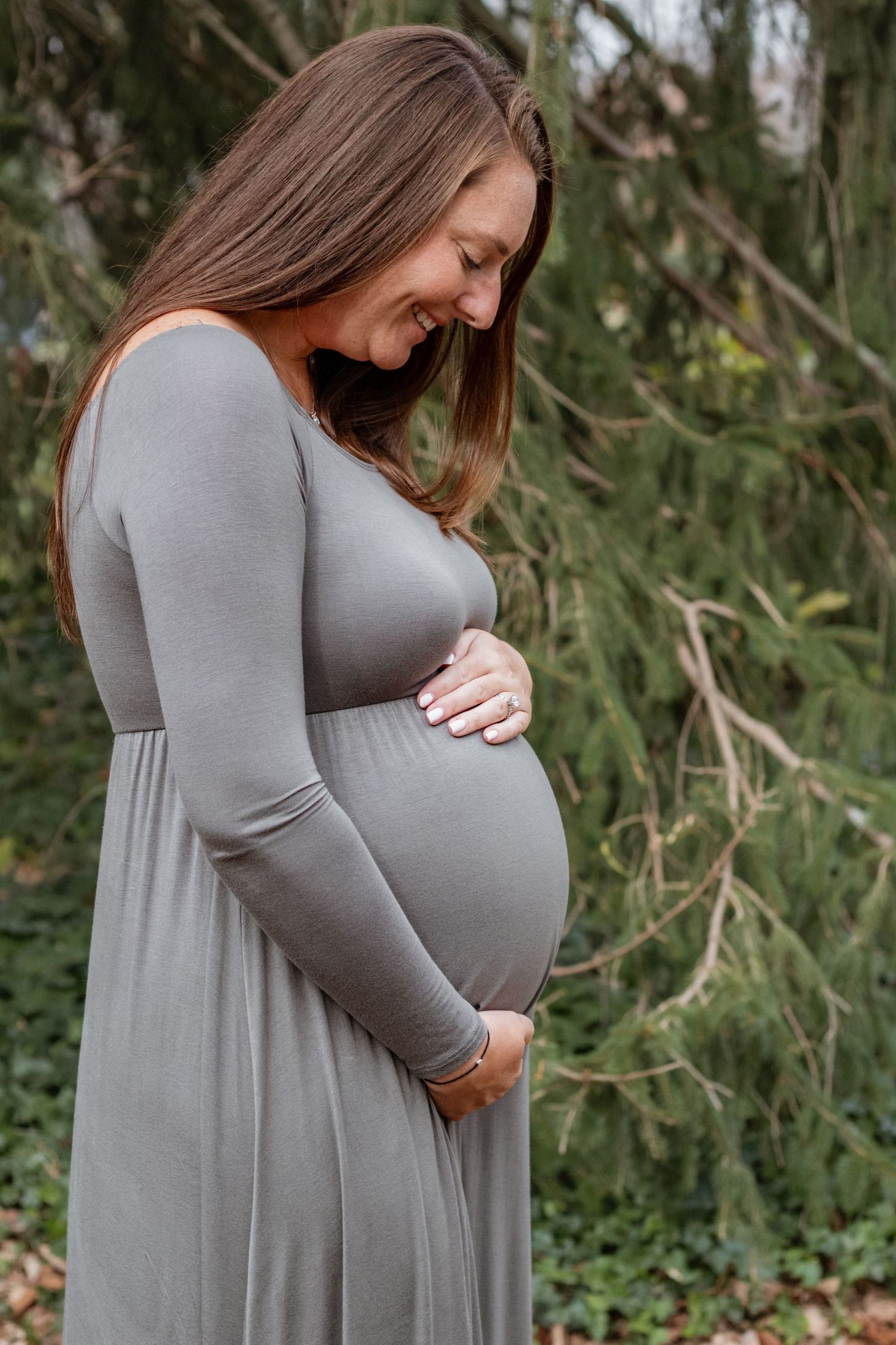 Woman in grey dress lovingly cradles her pregnant belly in outdoor maternity photos.