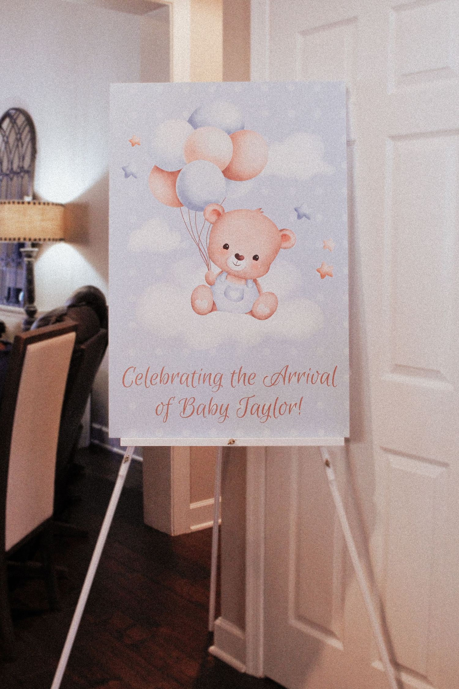 A baby shower welcome sign featuring a cute teddy bear with balloons in pastel colors.