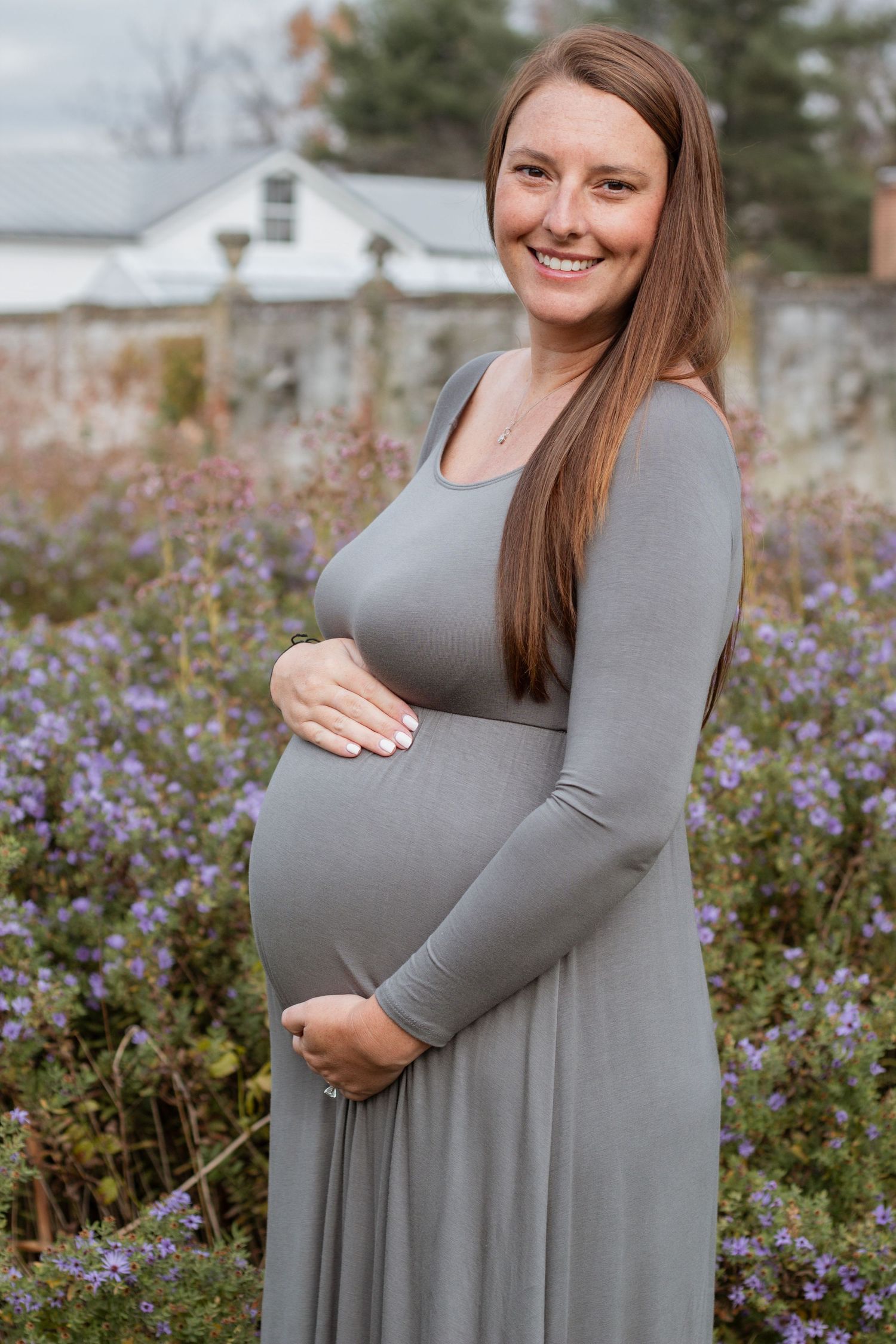 Maternity portraits in grey dress against purple wildflowers and natural scenery.