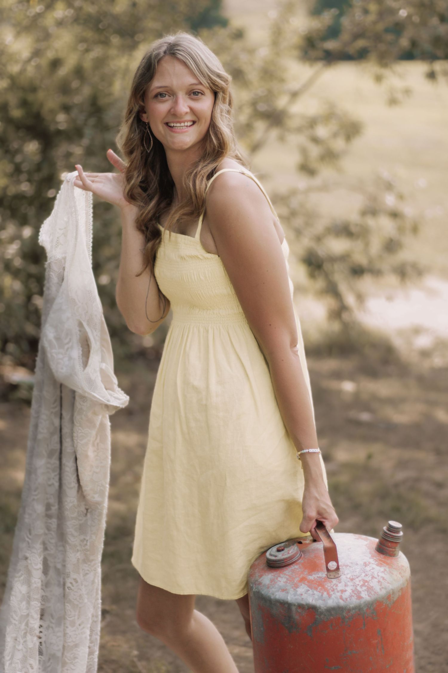A person in a yellow dress stands near a rustic red propane tank outdoors.