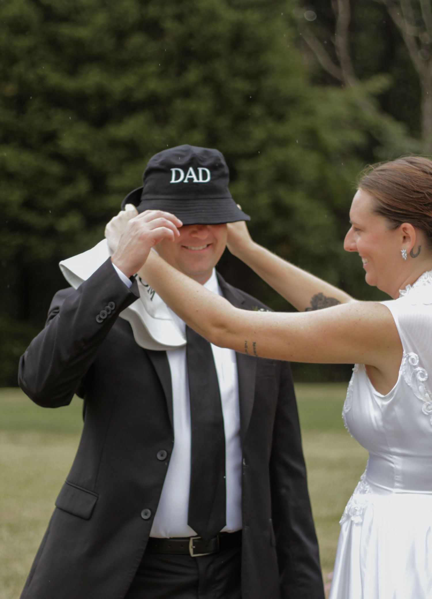 Playful wedding moment with couple dancing outdoors, groom wearing hat labeled 'DAD'.