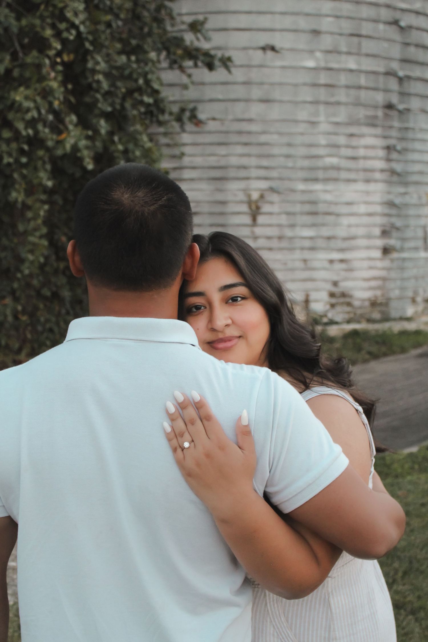 Engagement couple embracing outdoors near stone wall during photo session.