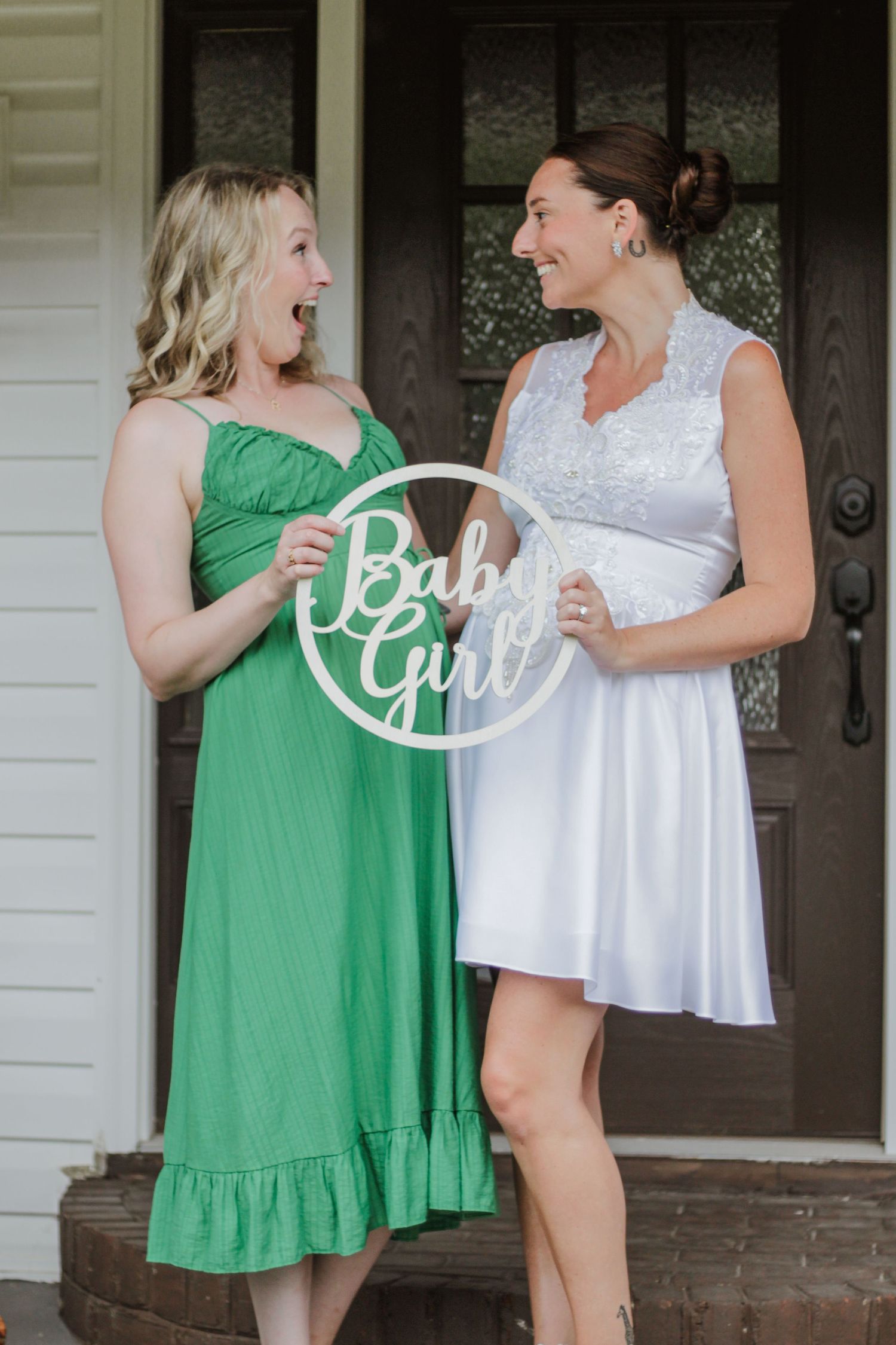Two people in contrasting white and green dresses laughing together on a porch.