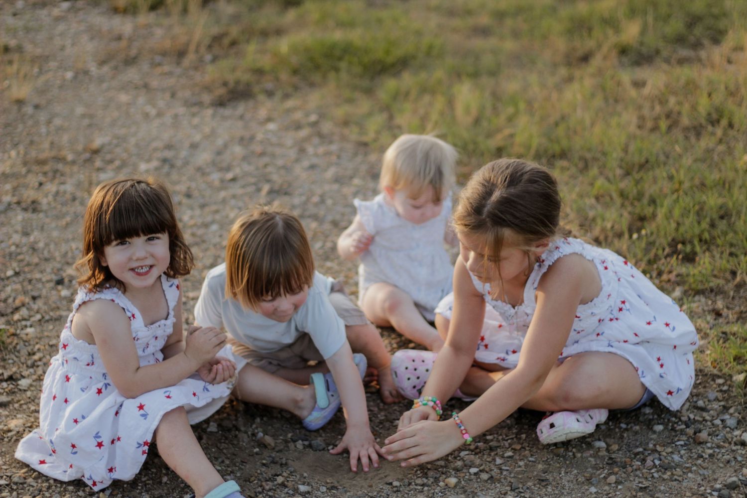 Group of children in white dresses sitting together outdoors.