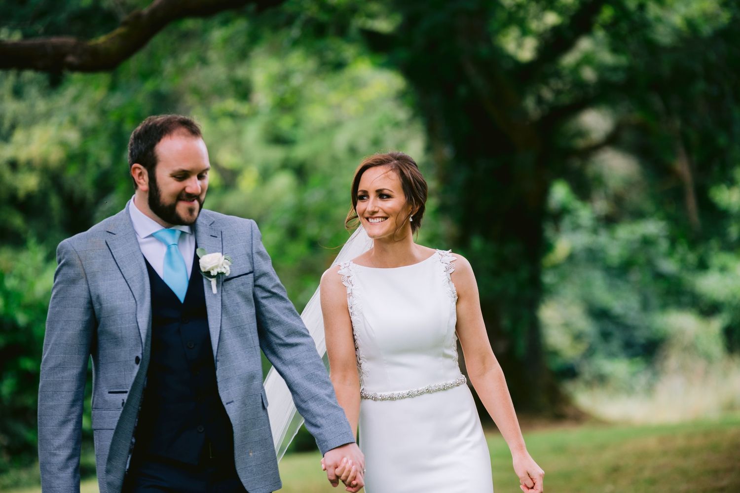 Happy newlywed couple holding hands and walking together through lush green garden setting.