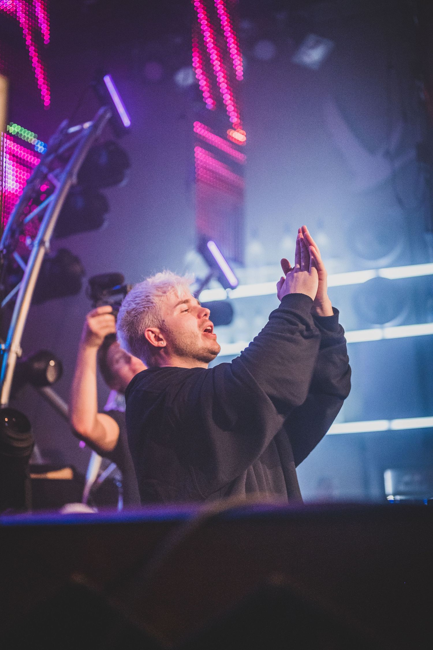 Blonde DJ with arms raised engaging crowd at energetic nightclub event with neon lights.
