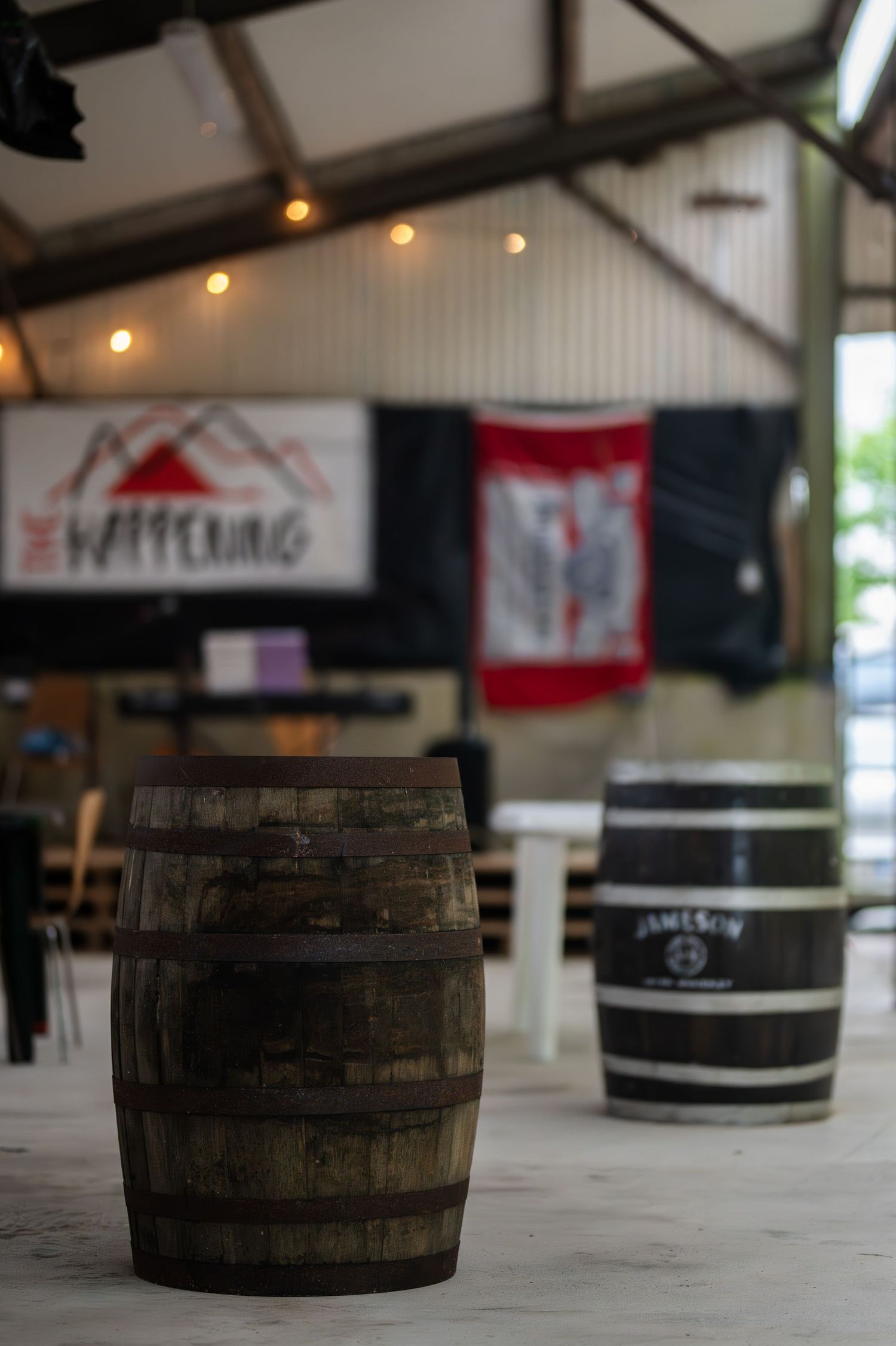 Rustic wooden whiskey barrels on display inside a bar venue with string lights and decorative flags.