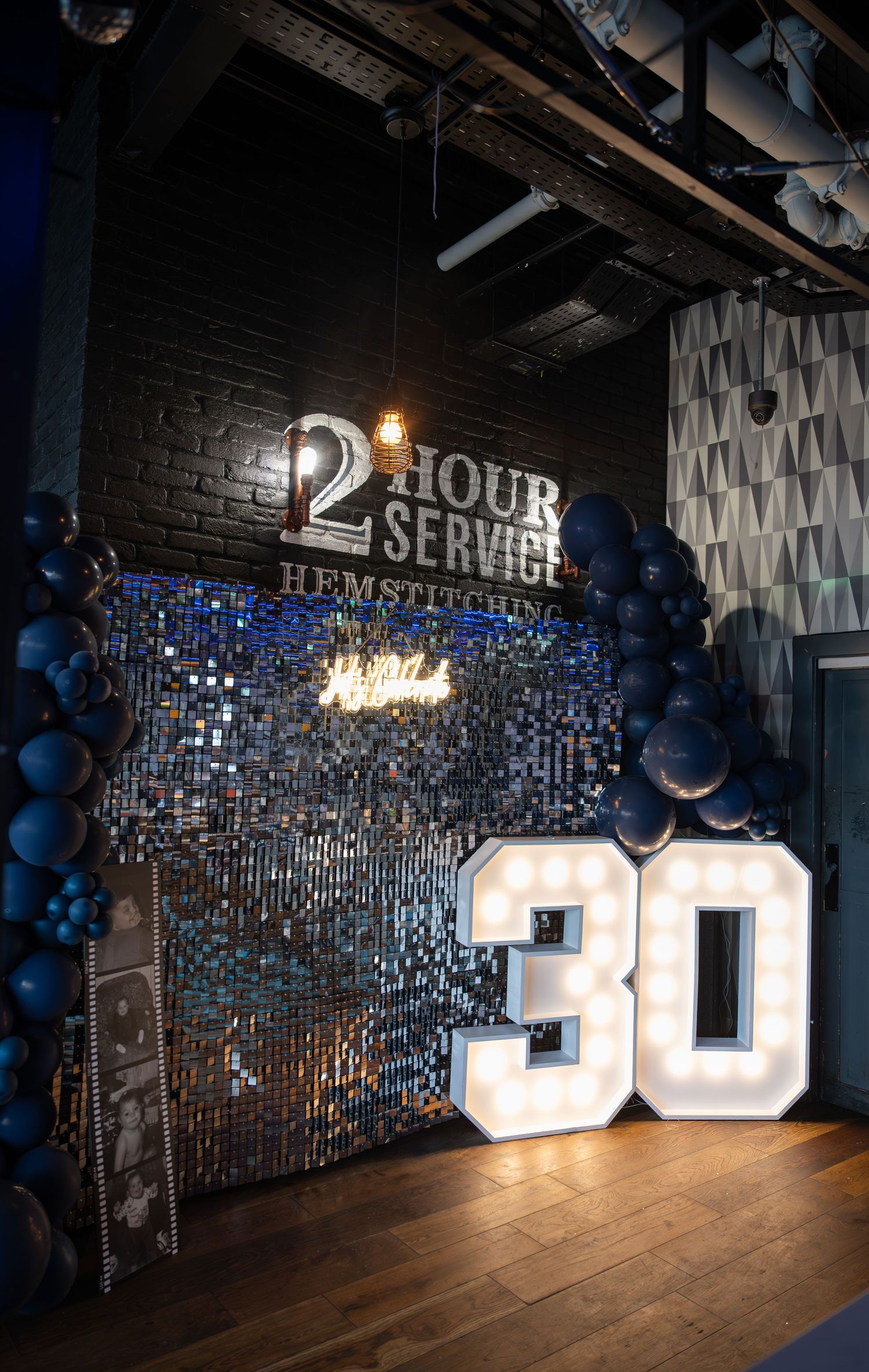 Glamorous 30th birthday party backdrop with navy balloons and illuminated marquee numbers.