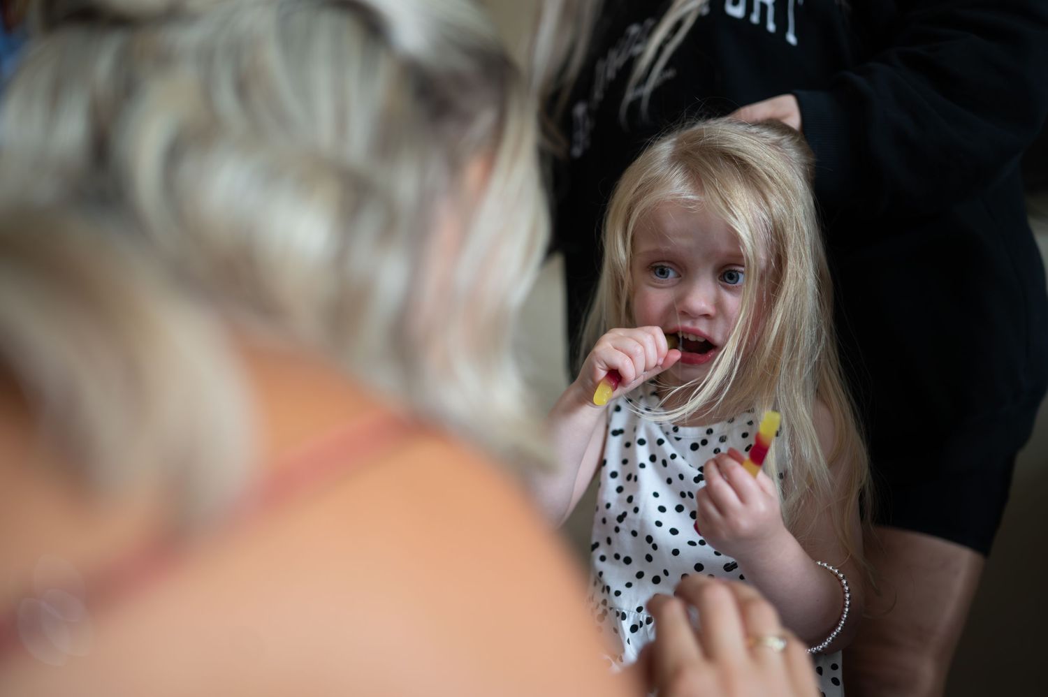 Blonde toddler girl in polka dot dress eating a snack at a wedding celebration.