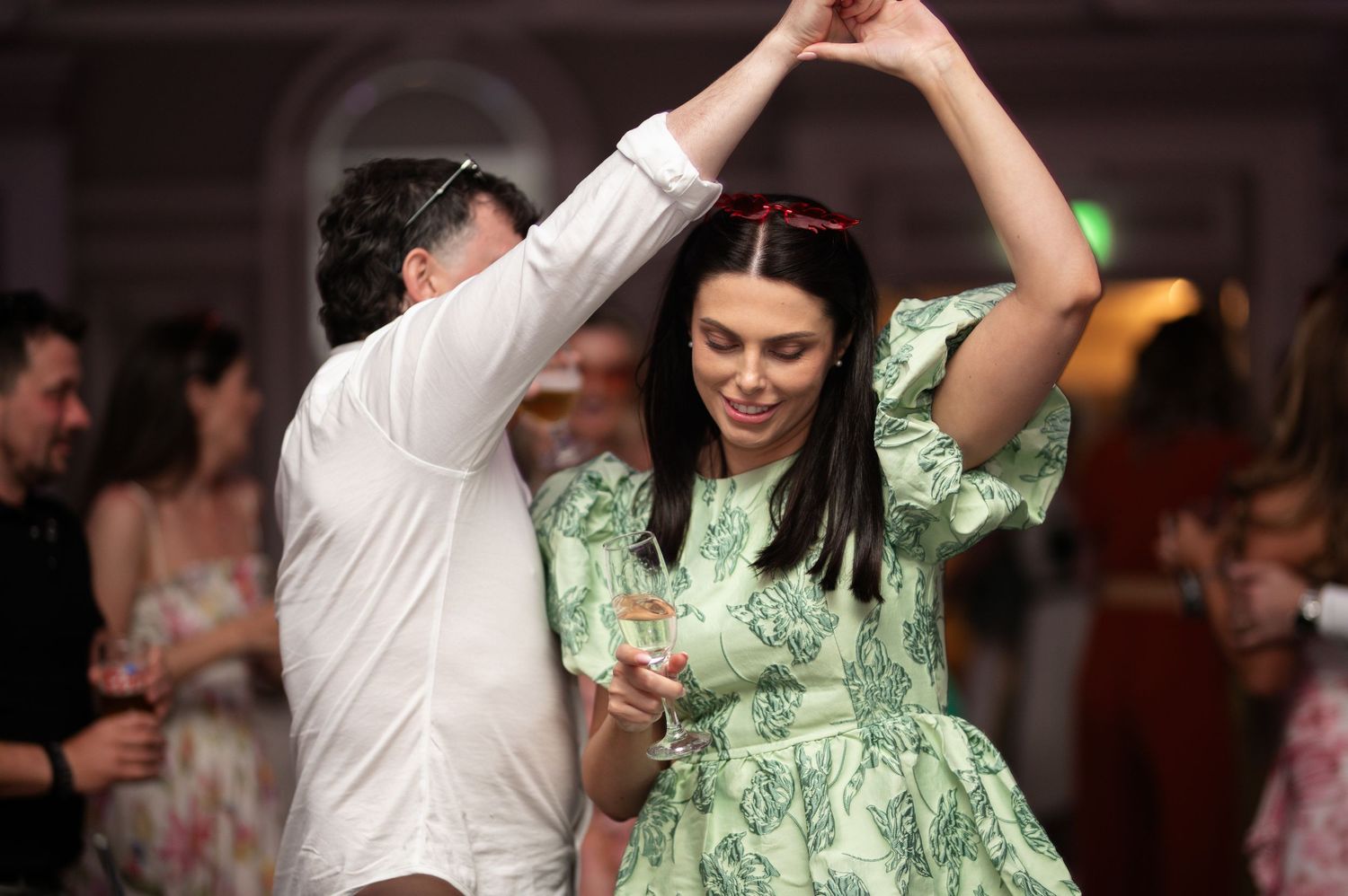 Couple dancing joyfully at wedding reception, woman in green floral dress twirling under mans arm.