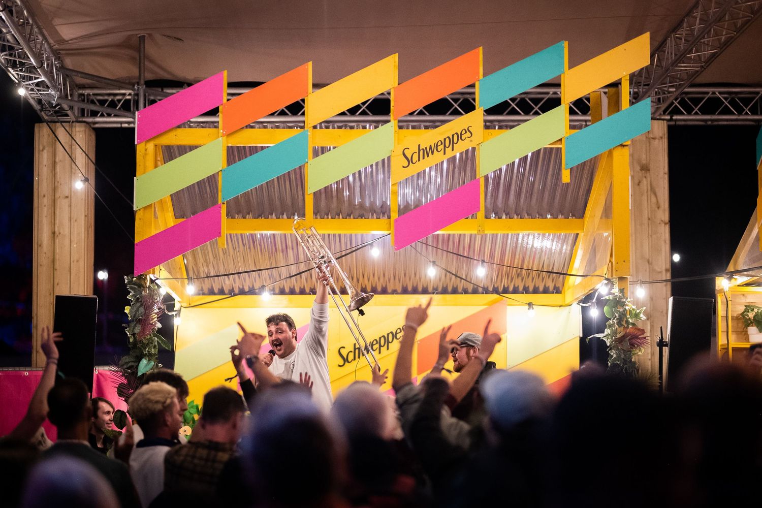 Colorful Schweppes branded stage with bunting at an outdoor evening festival event.