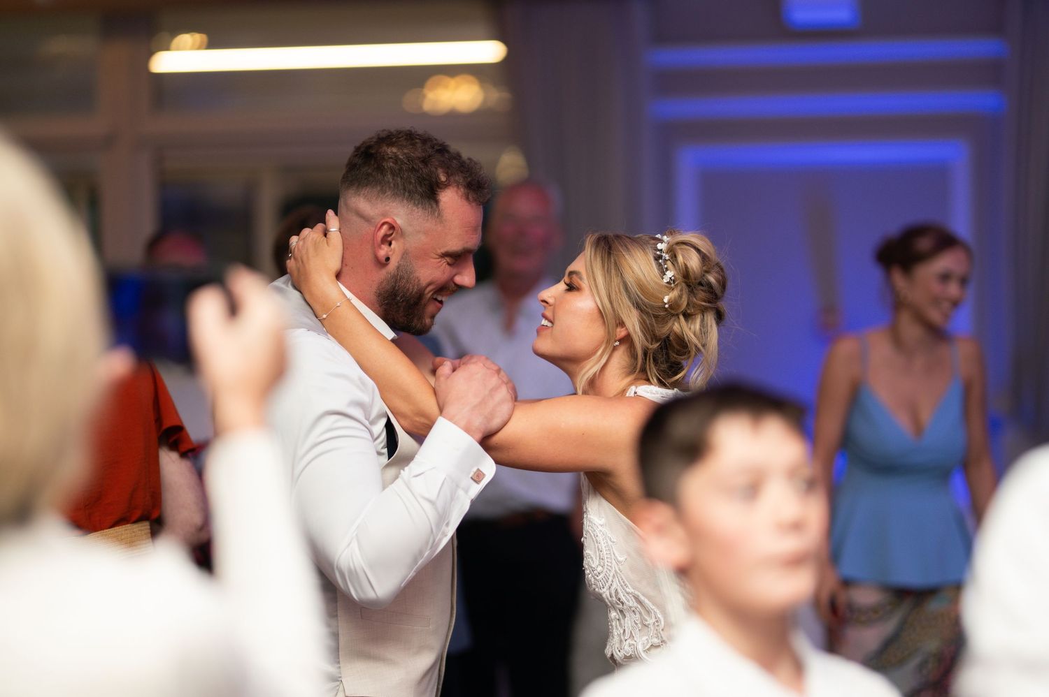 Bride and groom share a romantic first dance at their wedding reception with guests celebrating in the background.