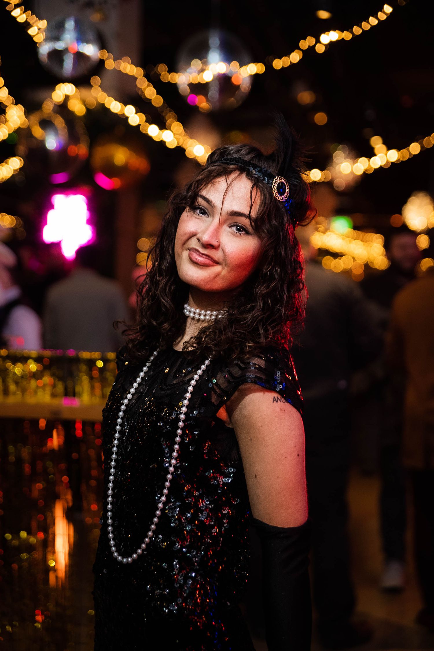 Woman in 1920s flapper costume with pearl necklace posing at a glamorous themed party.