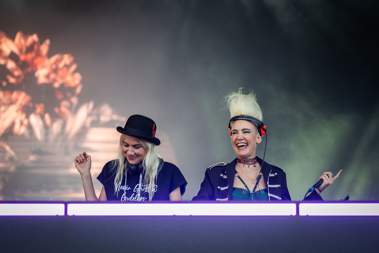 Two female DJs performing energetically on stage with dramatic lighting at a music festival.