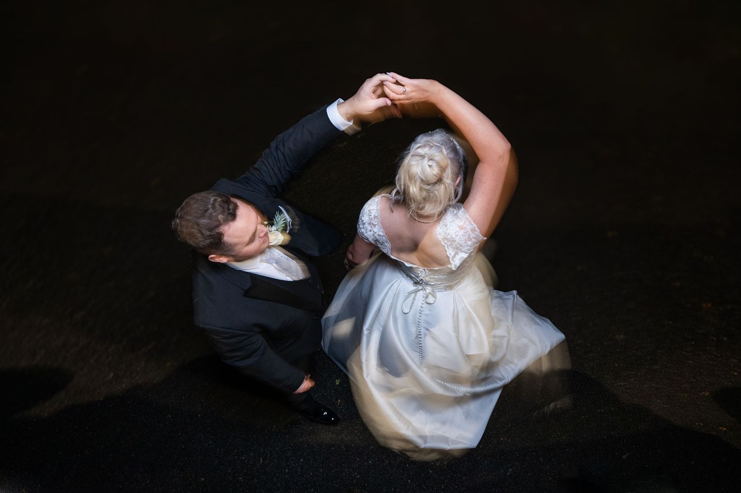 Aerial view of a bride and groom dancing elegantly on a dark floor at their wedding reception.