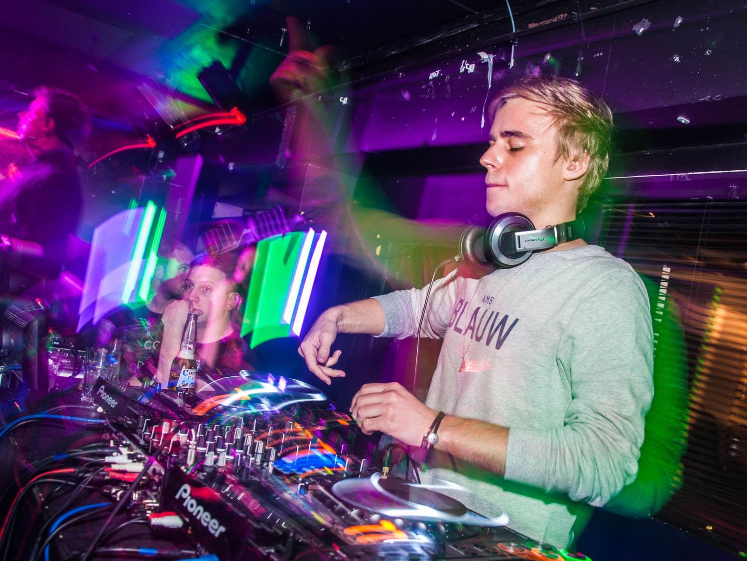 DJ performing at a nightclub with neon lights and Pioneer DJ equipment during a live set.
