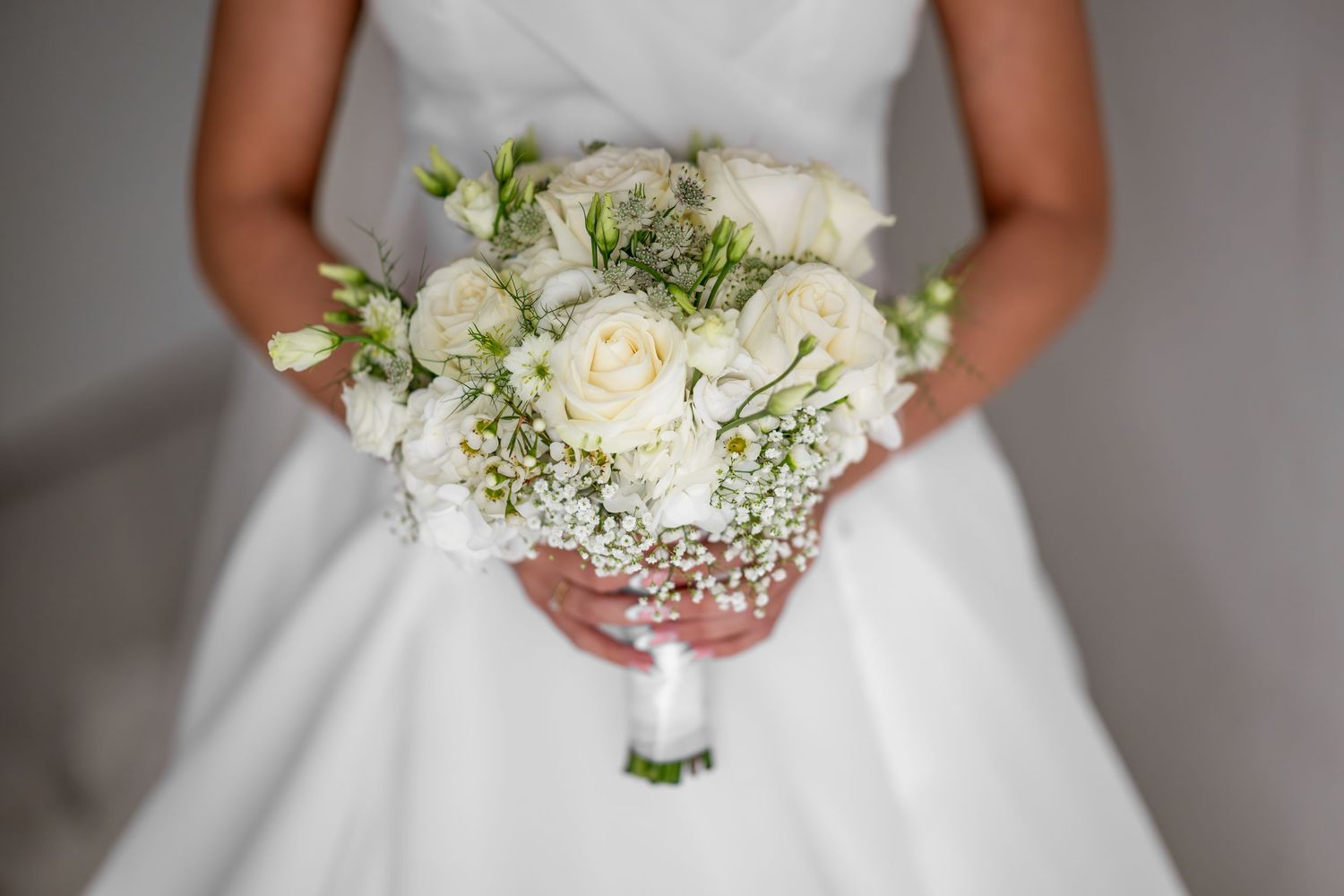 Bride in white dress holding elegant bridal bouquet of white roses and baby's breath at wedding ceremony.