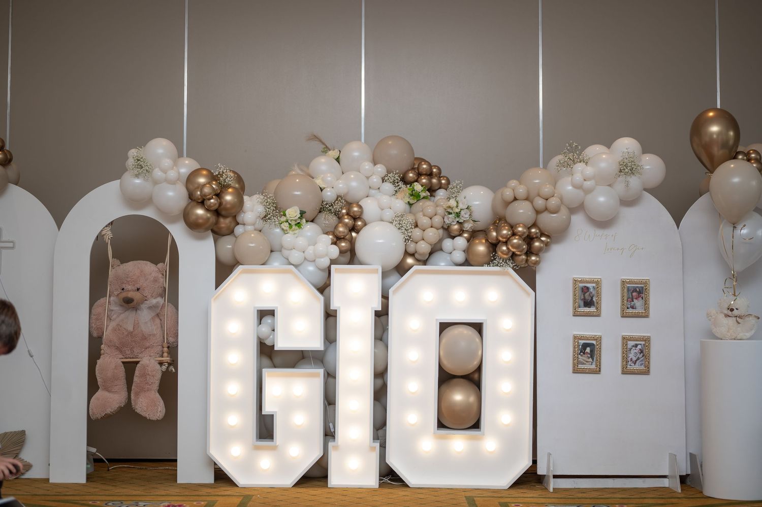 Marquee letter lights spelling GIO with balloon garland in gold, white, and blush tones for a birthday celebration.