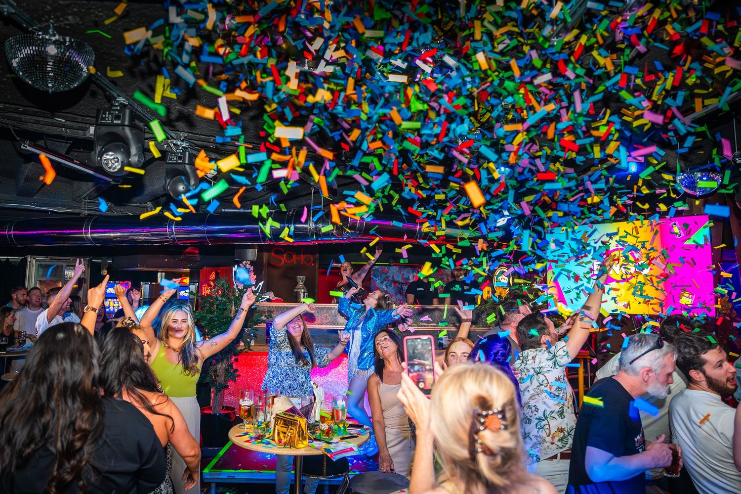 Energetic party scene with colorful confetti raining down on dancing guests in a vibrant venue.