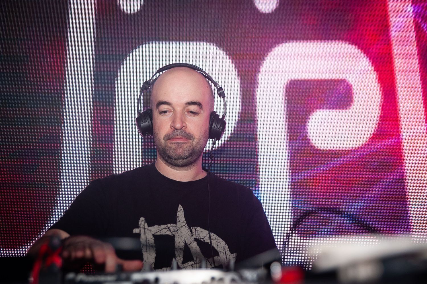 Male DJ wearing headphones performing at nightclub with colorful stage lighting.