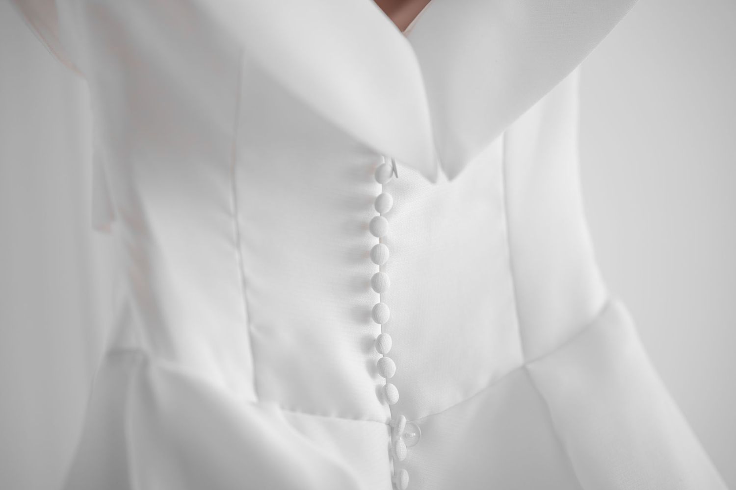 Close-up of an elegant white satin blouse featuring delicate button detailing along the front placket.