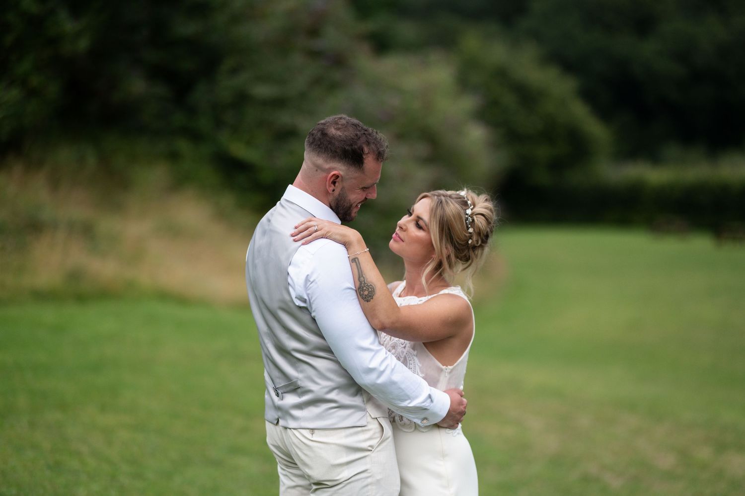 Bride and groom embracing tenderly in a green meadow during their outdoor wedding celebration.