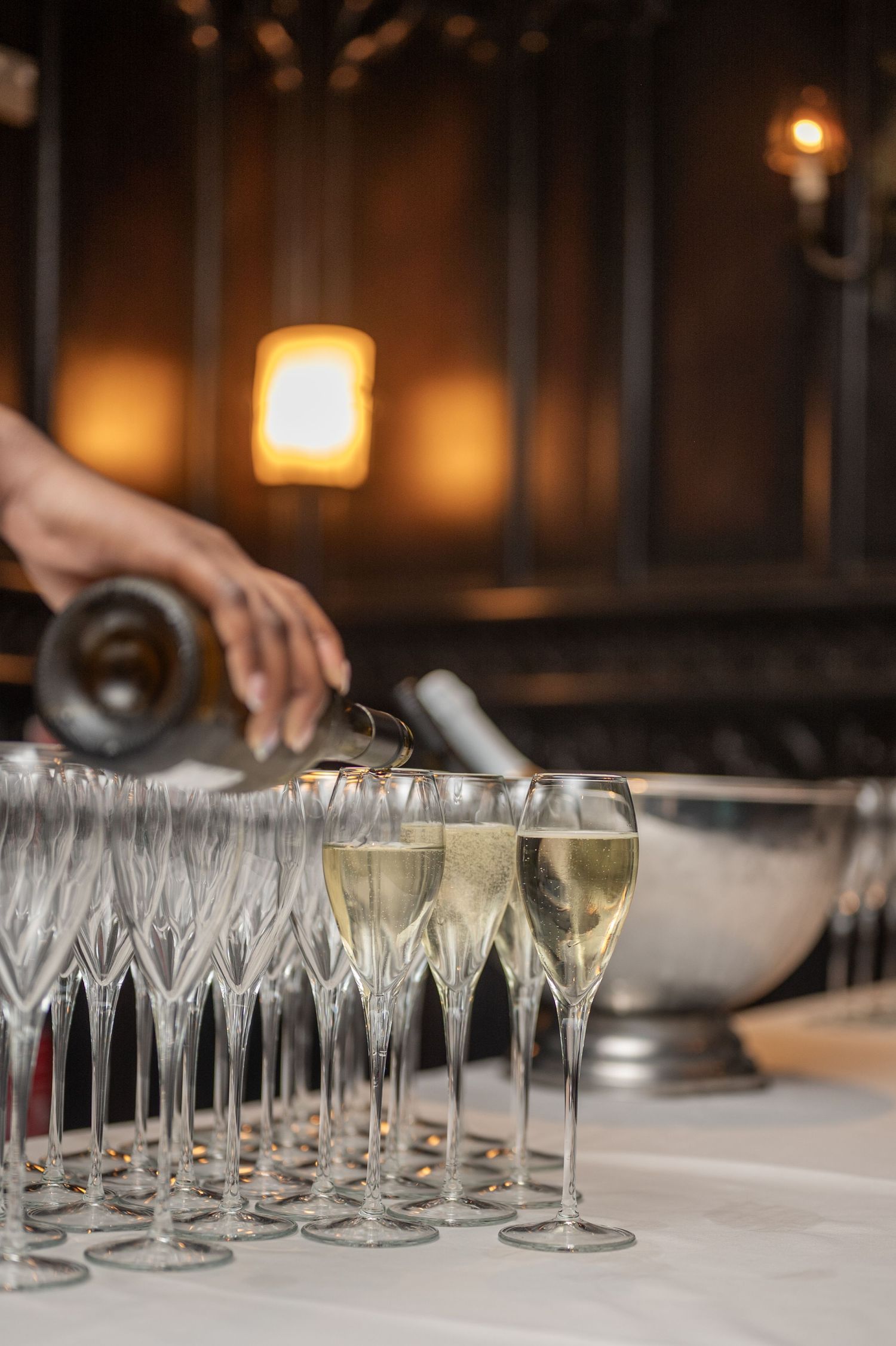 Bartender pouring champagne into rows of crystal flute glasses at luxury event reception.