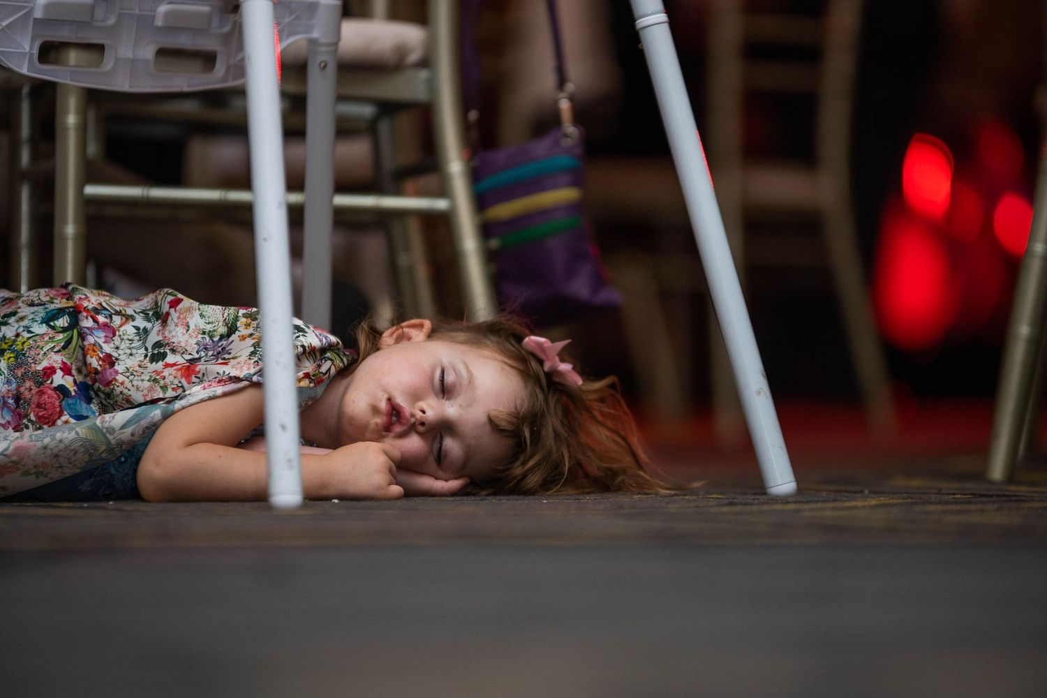 Tired young child sleeping on the floor under chairs at a wedding reception.