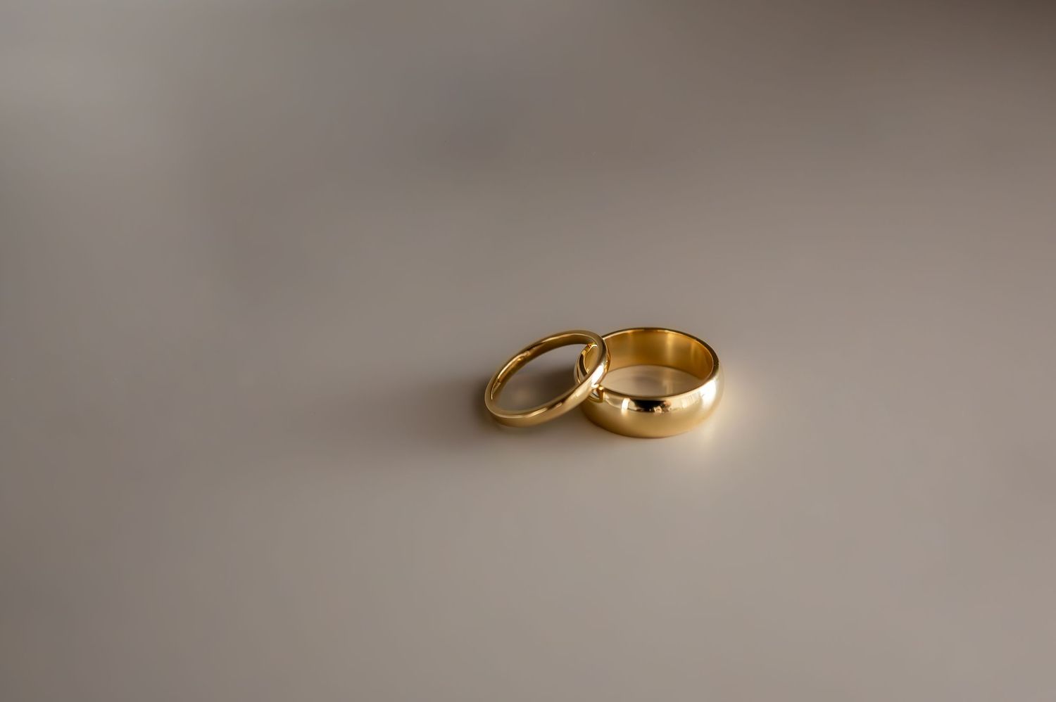 Two gold wedding bands resting together on a light gray surface, symbolizing love and commitment.
