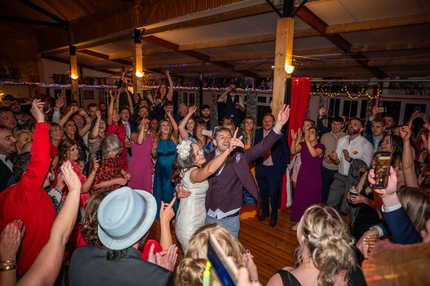 Bride and groom celebrated by cheering guests on a packed wedding dance floor.