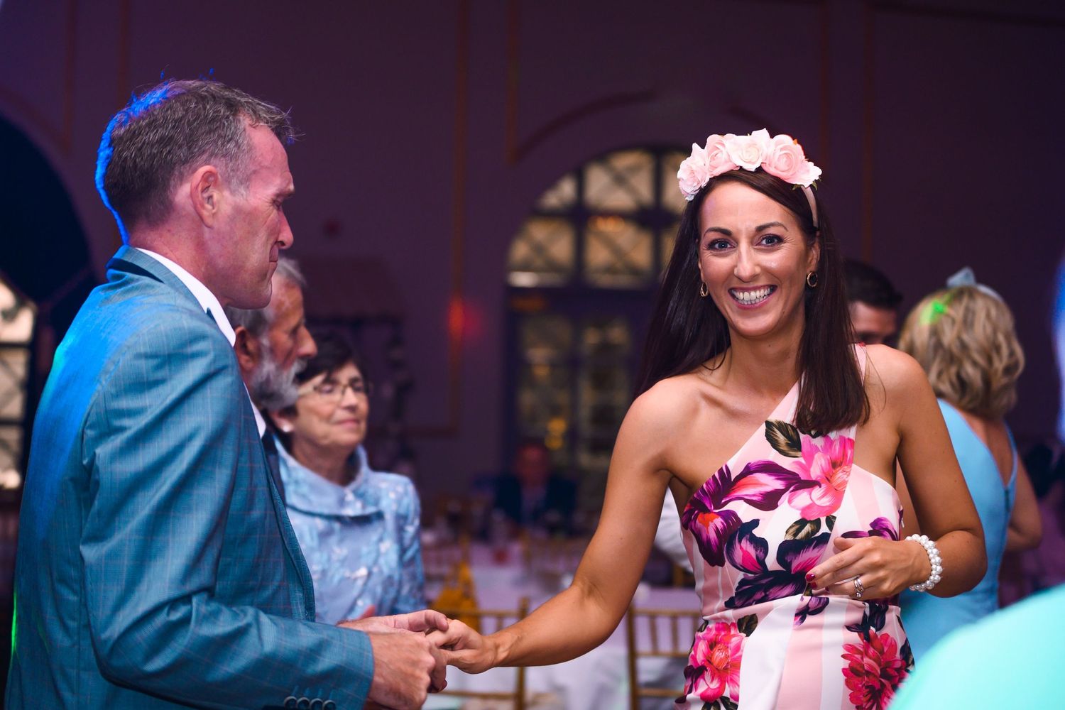 Woman in floral dress wearing flower crown dancing at a wedding reception.