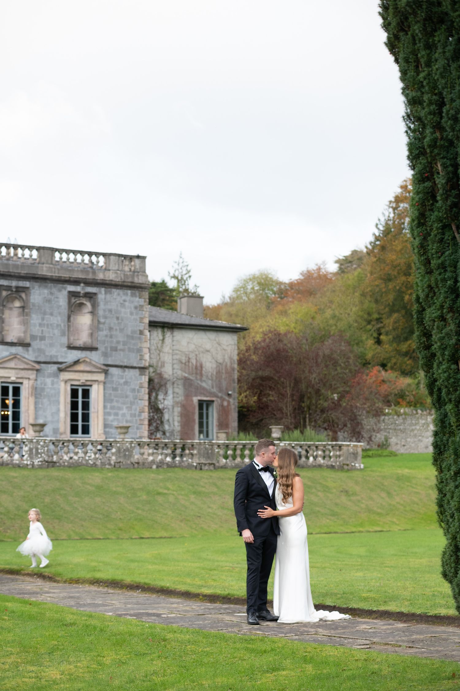 Bride and groom share a romantic moment on a garden path outside a grand stone manor house on their wedding day.