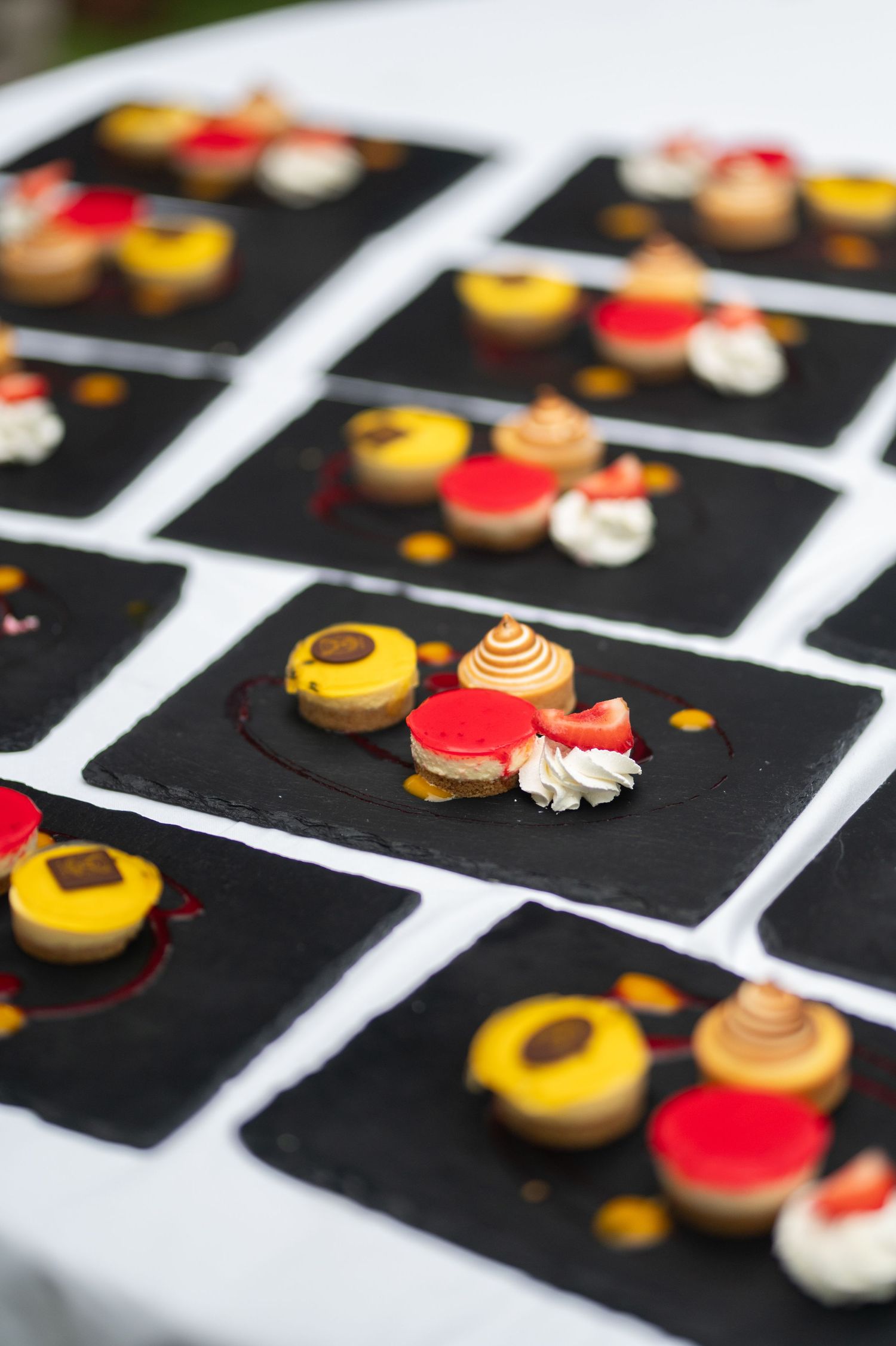 Elegant mini desserts with colorful toppings arranged on black slate boards at a wedding reception.