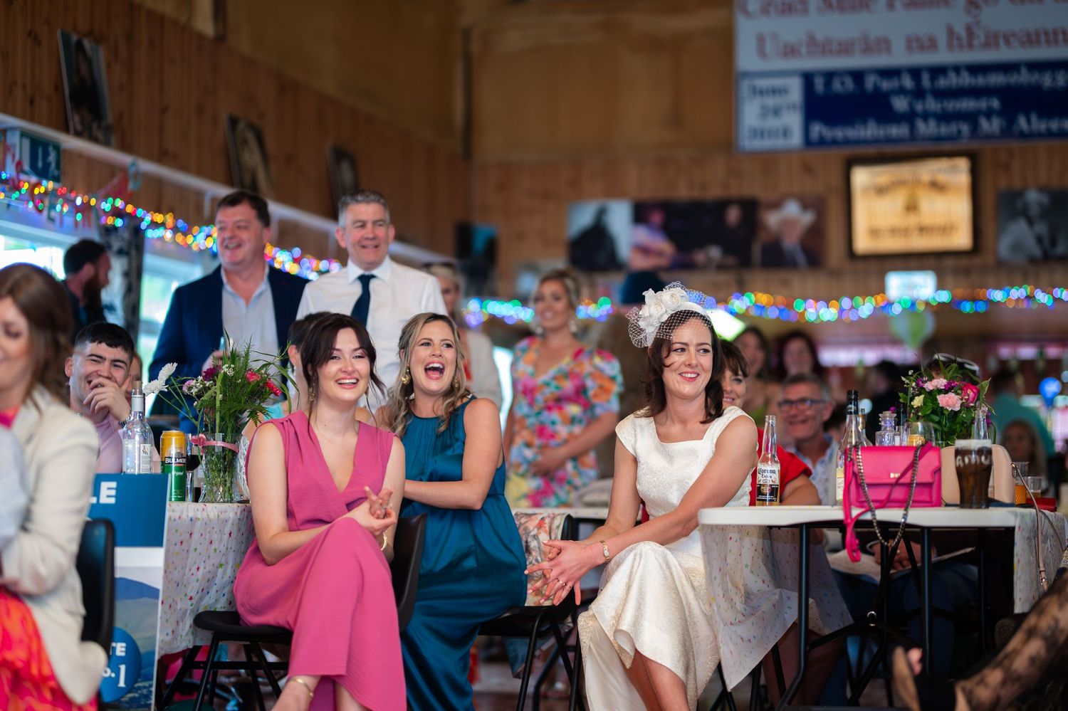 Women laughing and celebrating at a colorful indoor wedding reception in a decorated hall.
