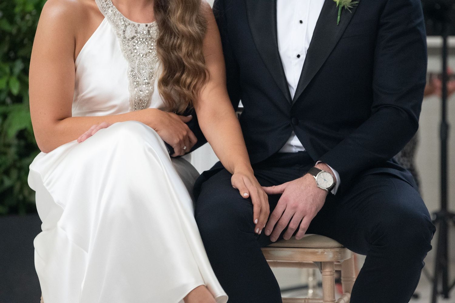 Elegant bride in white gown and groom in black tuxedo sitting together at a wedding ceremony.