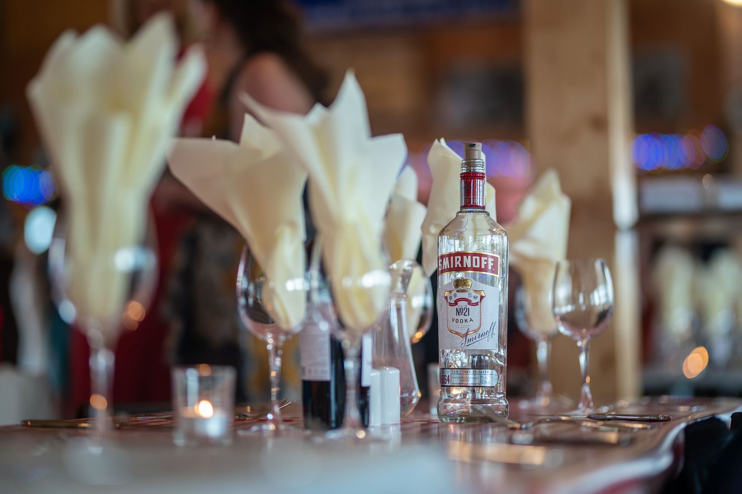 Smirnoff vodka bottle on a bar table with wine glasses and white napkin fans at an elegant event.