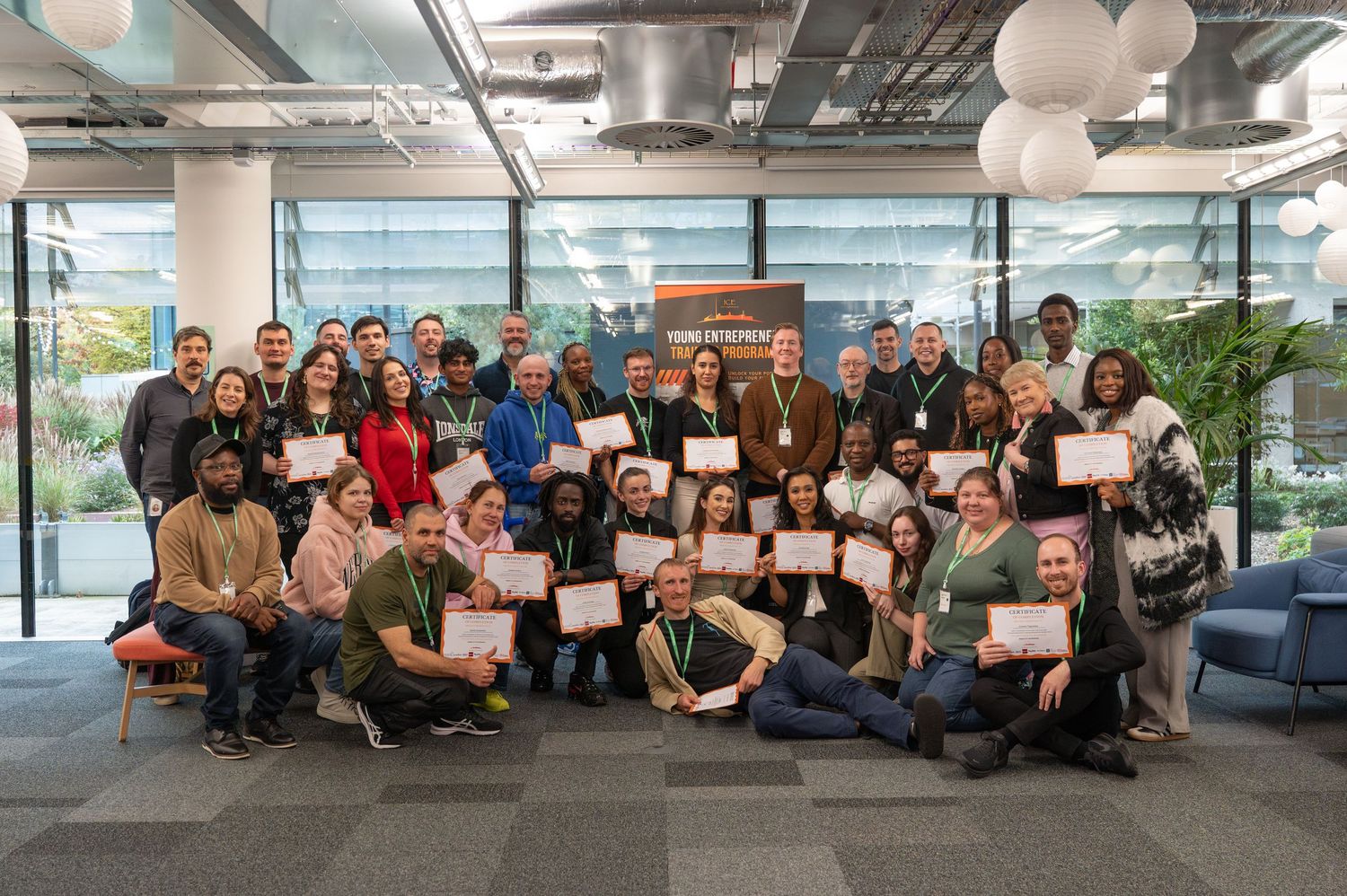 Large group of diverse professionals proudly holding certificates in a modern office space during an awards ceremony.