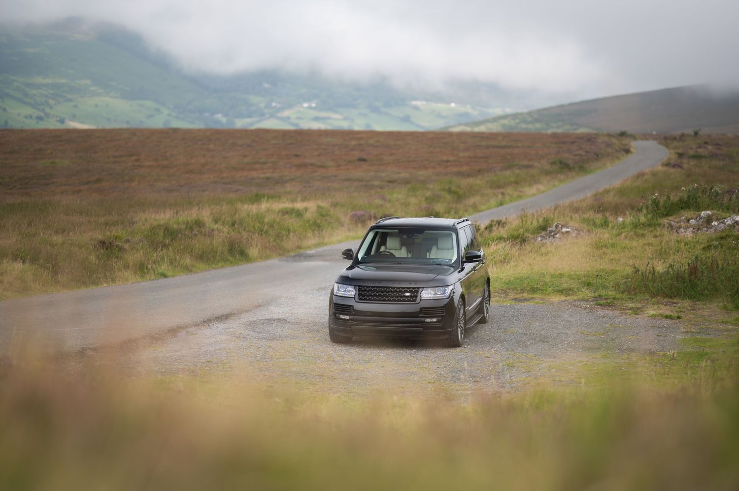 Black Range Rover driving on rural mountain in Wicklow road under overcast skies.