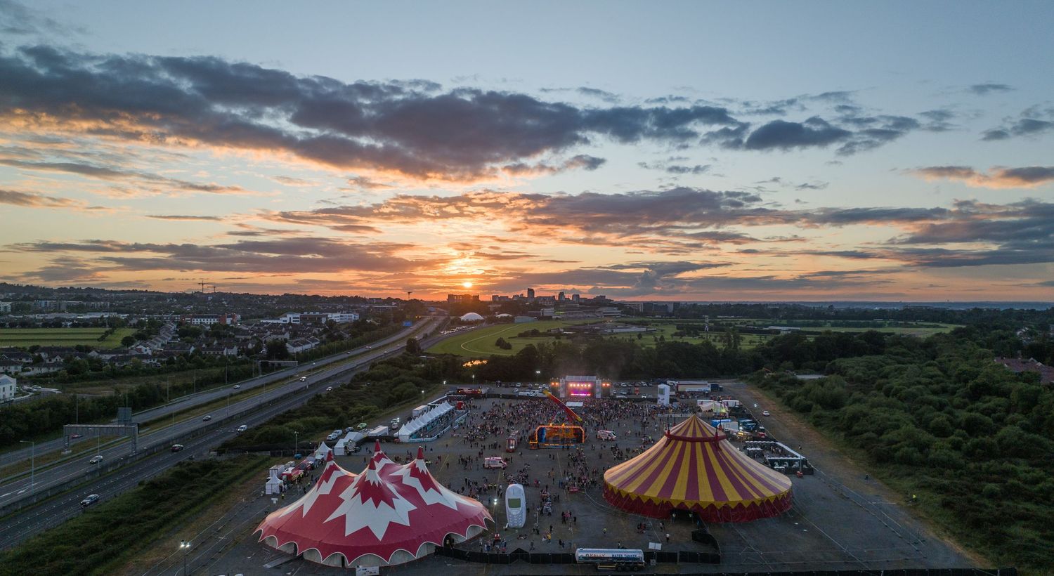 Aerial sunset view of a colorful circus festival with big top tents and crowds.