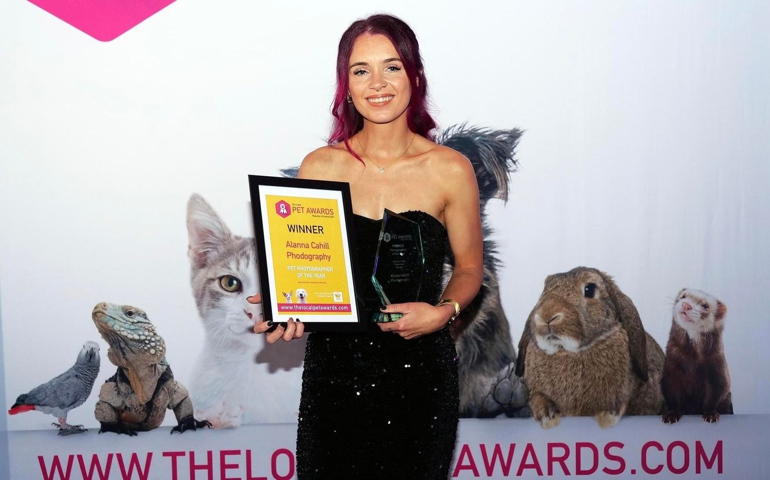 Young woman in black dress proudly holding award trophy at The Local Awards ceremony.