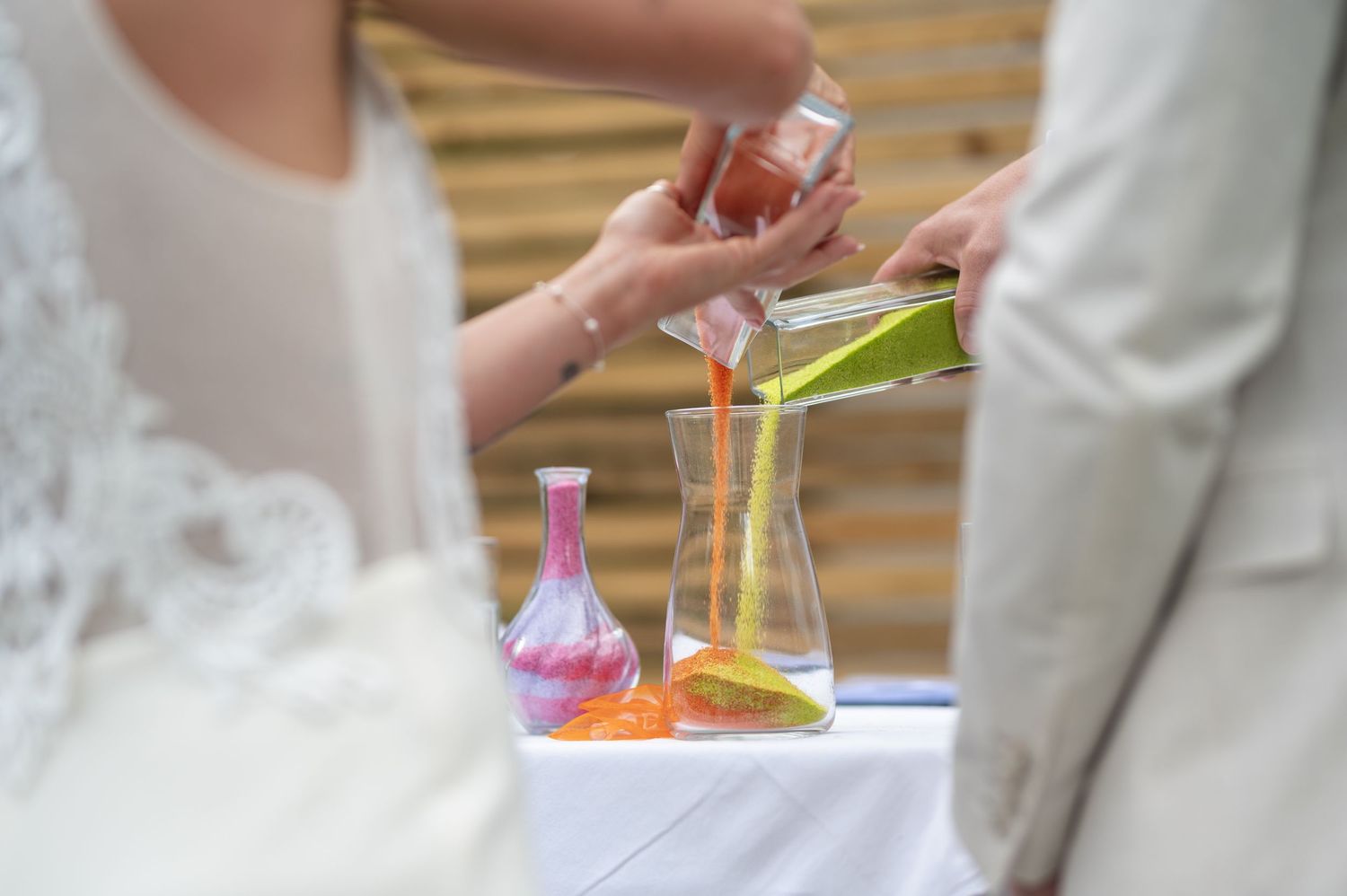 Bride and groom performing unity sand ceremony, pouring colorful sand into glass vase at wedding altar.
