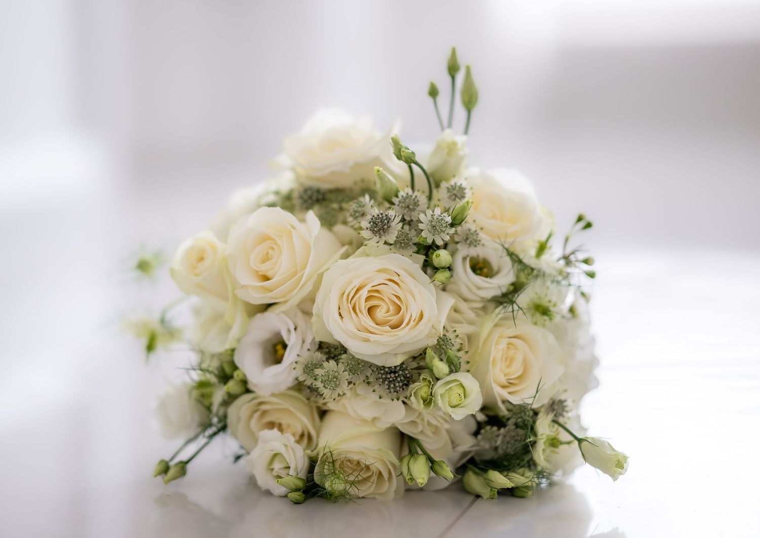 Elegant bridal bouquet of white roses and green accents on a white surface.
