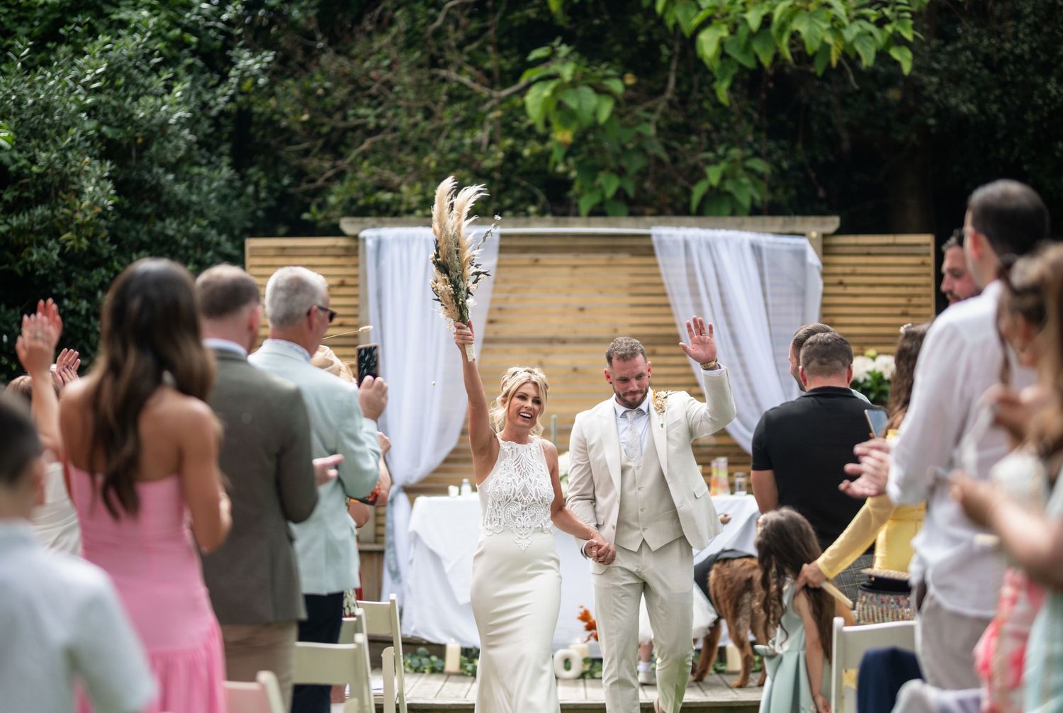 Joyful newlyweds walking back down the aisle celebrating after outdoor garden wedding ceremony.
