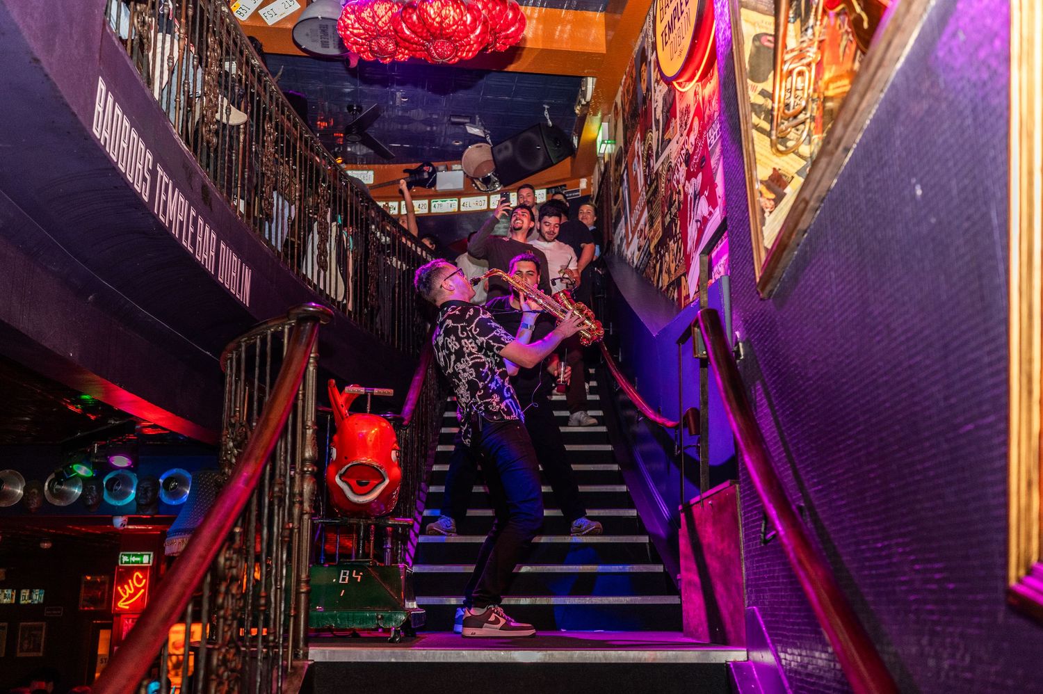 People posing on colorful neon-lit staircase inside a vibrant nightclub venue.