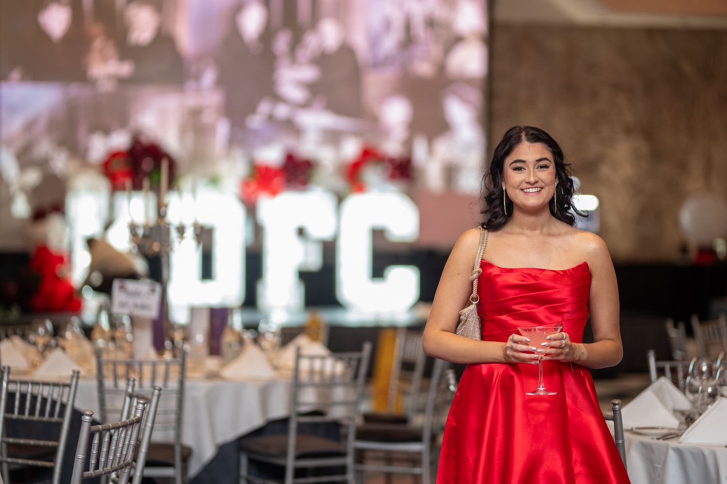 Young woman in red strapless gown at elegant KDFC gala dinner event with decorated tables.