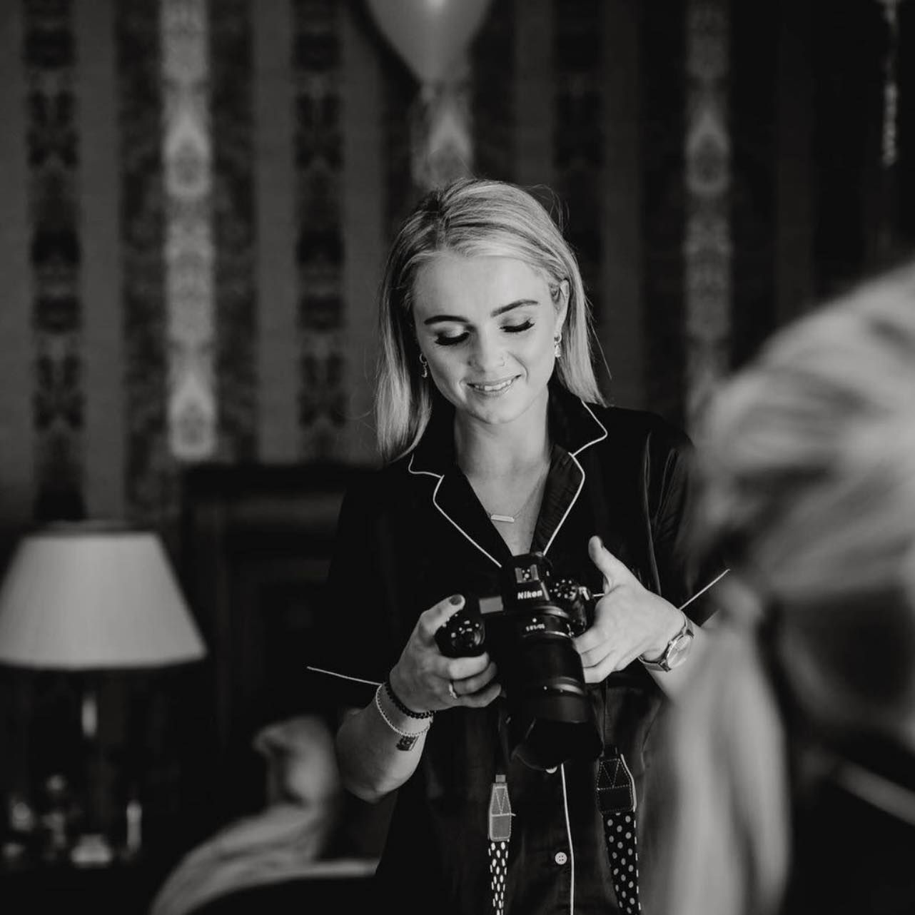 Blonde female photographer smiling while reviewing shots on camera in elegant interior.